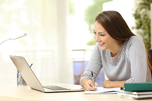 studentessa seduta alla scrivania che guarda il laptop e prende appunti