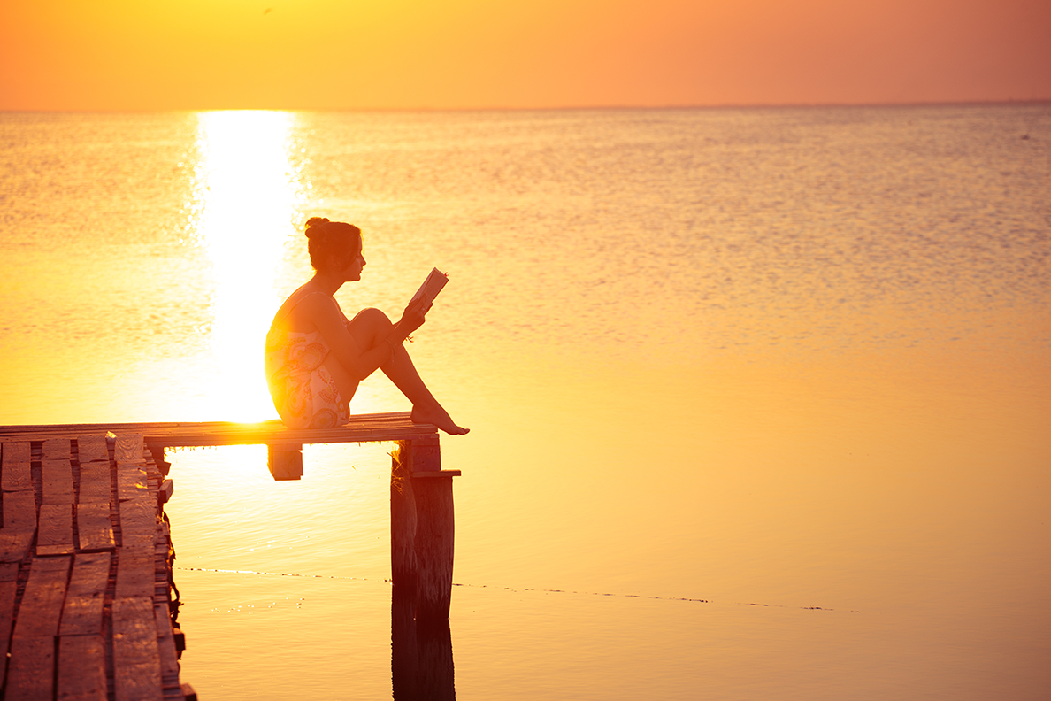ragazza seduta sul molo che legge un libro al tramonto